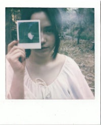 a woman holding up a polaroid in the woods